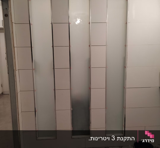 שלושה לוחות זכוכית חלבית מותקנים בקיר אריחים
